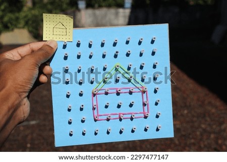 Geoboard made from cardboard at home with a picture of drawing made using elastic band held in the hand. Educational toy from recycled materials