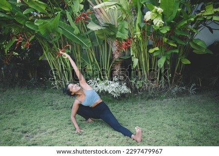 Full body of positive young ethnic female in activewear stretching and smiling while showing OK sign on green lawn in park