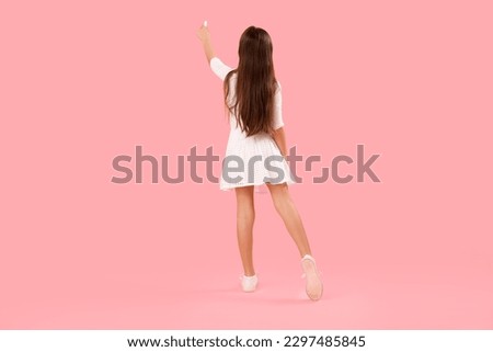 Little girl drawing with chalk piece on pink background, back view. Children's Day celebration Royalty-Free Stock Photo #2297485845