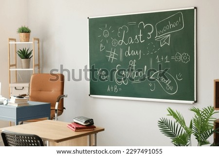 Blackboard with text LAST DAY OF SCHOOL and drawings on light wall in classroom Royalty-Free Stock Photo #2297491055