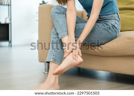 Close up woman leg knee pain feet. Female pain with ankle because walk too much. Massaging suffering knee foot. Pain at calves sitting on couch at home. Hands massage legs on sofa. Royalty-Free Stock Photo #2297501503