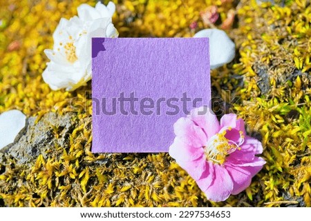 Mock-up of a purple Japanese paper message card decorated with pink and white plum blossoms and petals on a background of lots of moss