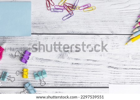 Blue sheets for notes, colored paper clips, colored pencils, paper clips and a proofreader for working in the office and studying at school on a light, wooden background.