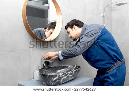 Close up photo of plumber with screwdriver fixing faucet in the bathroom. Handyman repairs a water tap	