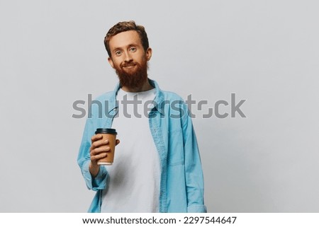 Man hipster with a cup of coffee with a smile on a gray background in a blue shirt and white t-shirt