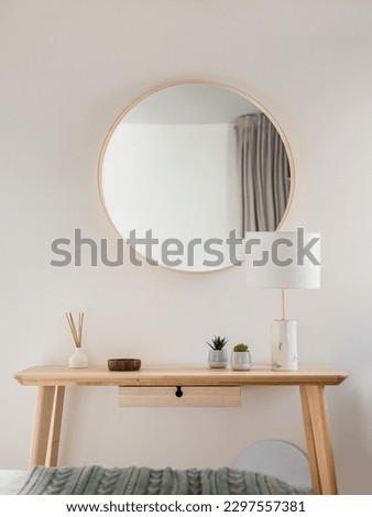 Close-up of a wooden table and a frame with mirror with stylish accessories in a young womans bedroom. The concept of stylish minimalist interior design in a new apartment. Copyspace Royalty-Free Stock Photo #2297557381