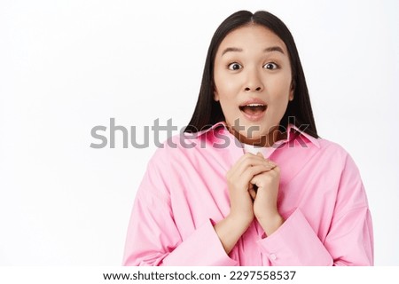 Close up portrait of asian girl looks hopeful and surprised, stands amazed against white background. Copy space