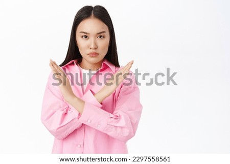 Stop. Serious korean woman shows prohibit, taboo sign, makes cross hands gesture, disapprove smth, stands over white background.