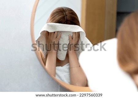 Young woman wiping her face with towel in front of the mirror in the bathroom Royalty-Free Stock Photo #2297560339