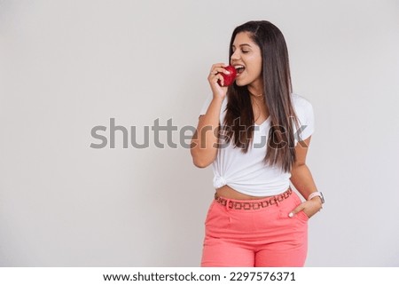 Beautiful Brazilian woman, white shirt and pink pants. advertising photo, eating apple.