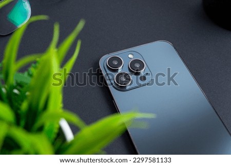 Phone backside with cameras and sensors. Phone laid on the black table and accused of plant green leaves