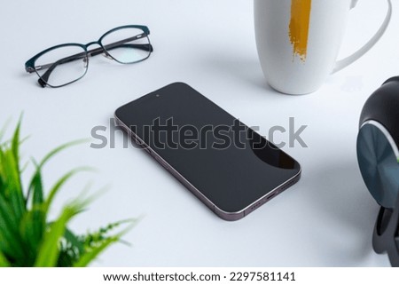 Phone placed beside office items like a headset, plant, glasses, and a coffee mug. Productivity and modern technology in a work environment composition