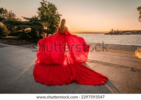 Sunrise red dress. A woman in a long red dress against the backdrop of sunrise, bright golden light of the sun's rays. The concept of femininity, harmony.