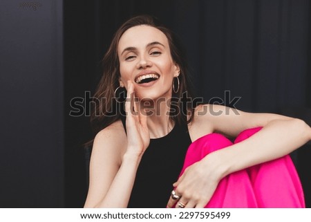 Photo of excited crazy girl hand near open mouth say tell information. Woman sitting at house outdoors, wear pink trousers, black tank top, look happy, secret informations or whisper.