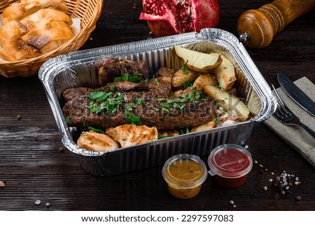 Grilled meat in plate. Meat shish kebab with herb and spices. Hot portion barbecue with beef, pork, chicken, potatoes, onions and sauces in box. Royalty-Free Stock Photo #2297597083