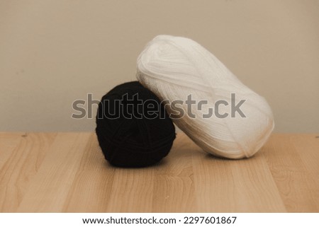 A couple of balls of yarn, one yarn  ball white and one yarn ball black. Photographed on a light wood against a light wall. Image for crafting like crochet or knitting.