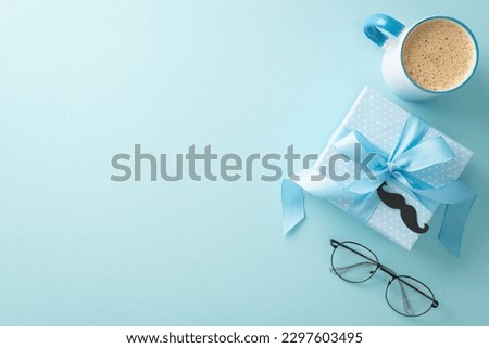 Father's Day arrangement with class. Overhead shot of spectacles, mustaches, gift box, coffee mug, and blank space for text on pastel blue background Royalty-Free Stock Photo #2297603495
