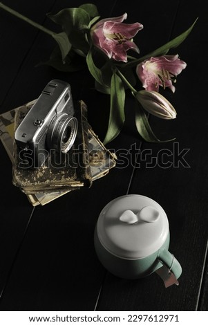 A simple still life with a vintage camera, some flowers and a cup of tea with a lid