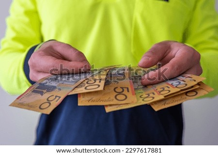 View of a tradesman in high visibility clothes holding australian dollar notes Royalty-Free Stock Photo #2297617881