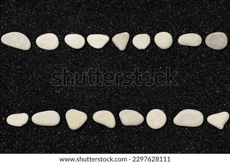 Black beach sand with lines of pebbles. Travel and vacations concept background with space for your own text. Top view, flat lay