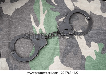 Handcuffs on a Camouflage background. Metal shackles isolated. Law. Limitation. Freedom. Security. Police bracelets. Military uniform.  Soldier textiles. The texture of the spots. Camouflage colors   
