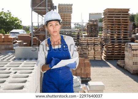 Asian woman manager working in an open air warehouse keeps records of construction materials, entering the data into the ..estimate