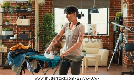 Frustrated woman ironing clothes and being angry at husband, wife needing help with household chores. Stressed tired person cleaning house and doing housekeeping work without man. Royalty-Free Stock Photo #2297640767