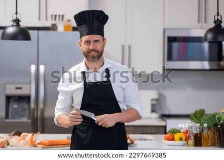 Man in cook apron and chef hat at modern kitchen preparing fish salmon. Handsome man is cooking fresh fish salmon seafood crab and shrimp and lobster in the kitchen at home.