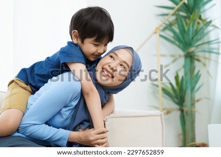 Happy cheerful Asian muslim family living together in a weekend, woman muslim embracing her lovely little son and smiling to camera. Modern muslim lifestyles concept. Royalty-Free Stock Photo #2297652859