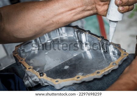 Auto mechanic applying black high-temp RTV silicone gasket maker to oil pan flange. Royalty-Free Stock Photo #2297698259