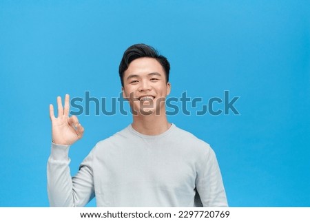 Portrait of handsome excited man smiling and showing ok sign at camera isolated over blue background