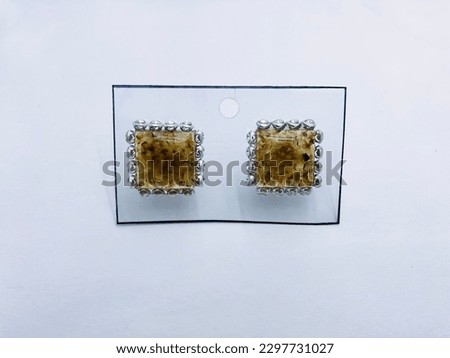 A brown colour,square shape two earrings on a white background.They have silver border.Inside of the earrings have brown colour small items.This earrings made of resin material.They are so beautiful.