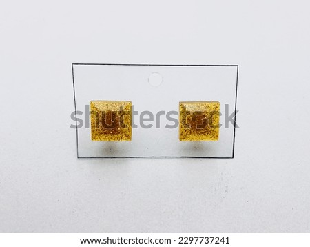 A yellow colour, square shape two earrings on a white background. The inside of the earrings have yellow colour glitter powder.This earrings made of resin material. This earrings are really beautiful.