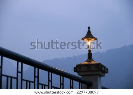 turned on black old fashioned garden lamp on railing with warm yellow light against blue sky. copy space