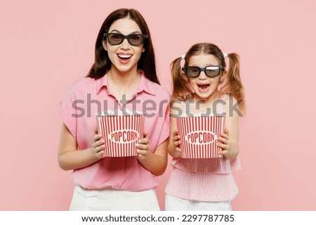 Young woman wear casual clothes with child kid girl 6-7 years old in 3d glasses watch movie film hold bucket of popcorn in cinema. Mother daughter isolated on plain pink background. Family day concept Royalty-Free Stock Photo #2297787785