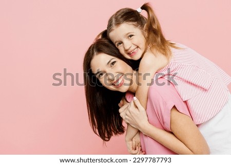 Happy woman wear casual clothes with child kid girl 6-7 years old. Mother, giving piggyback ride to joyful daughter, sitting on back isolated on plain pastel pink background Family parent day concept Royalty-Free Stock Photo #2297787793