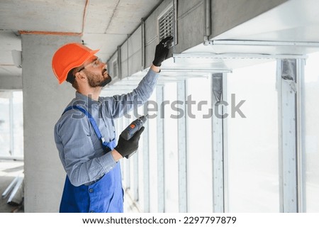 Industrial Theme. Warehouse Heating and Cooling System Installation by Professional Caucasian Technician. Commercial Building Ventilation Rectangle Canals. Air Distribution Royalty-Free Stock Photo #2297797879