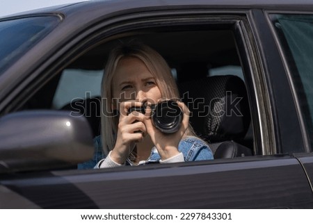Young blonde woman takes pictures sitting in a car. Concept of journalism, detective, papparation