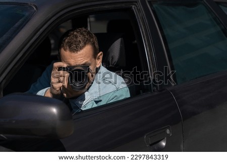 Paparazzi men or guy in his car and takes pictures of famous person.Spy with camera in car. Private detective or paparazzi journalist sitting inside car, taking pictures with camera.