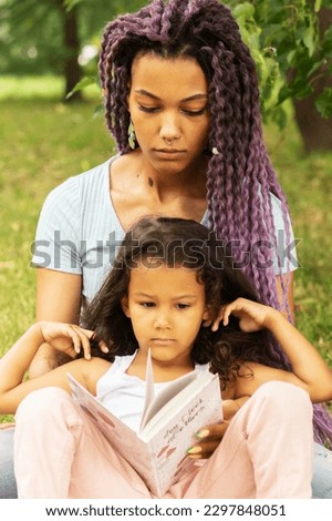 modern young african mother teaching daughter to read in the park, back to school, parent with child, preschool education