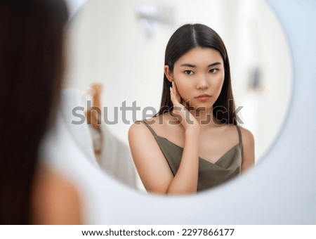 Portrait of attractive young woman looking at mirror. Beautiful girl enjoying her reflection, self-care concept. 