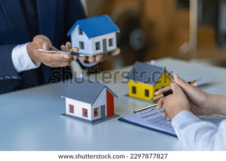 Real estate agents offer contracts to buy or rent housing. Businessman holding model small building house with property insurance at table in home sales office