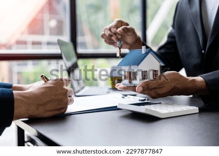 Real estate agents offer contracts to buy or rent housing. Businessman holding model small building house with property insurance at table in home sales office