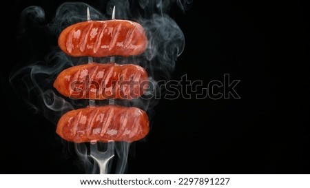 Grilled sausages with smoke. Fried sausages on fork, black background. Place for text