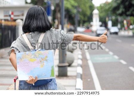 Back view of female traveler raising hand for calling taxi while holding map at the sidewalk 