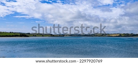 There are a lot of white cumulus clouds in the sky over the sea coast on a summer day. Seaside Irish landscape. Blue sea under blue sky and white clouds