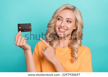 Photo of cheerful positive lady dressed orange t-shirt looking showing finger credit card isolated teal color background