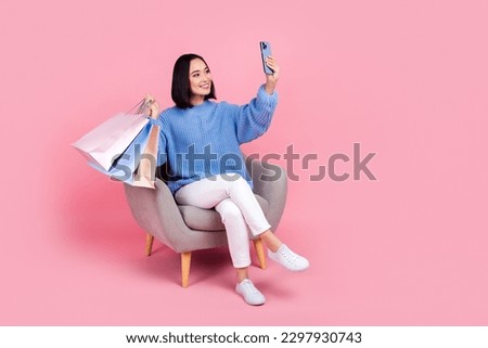 Full size photo of charming girl sit chair hold smart phone boutique bags make selfie isolated on pink color background
