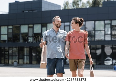 cheerful dad hugging happy teenage son while walking from mall with shopping bags Royalty-Free Stock Photo #2297938373