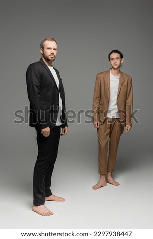 full length of well dressed father and teenage son in suits standing together on grey Royalty-Free Stock Photo #2297938447